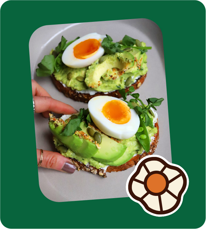 A person holding a perfectly cooked egg atop a slice of avocado toast on a wooden table