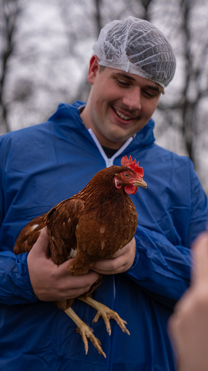 A man smiling while holding a chicken in his arms, showcasing a friendly interaction with the animal